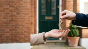 Close-up of a hand receiving house keys in front of a British home on completion day, symbolizing the legal transfer of property ownership