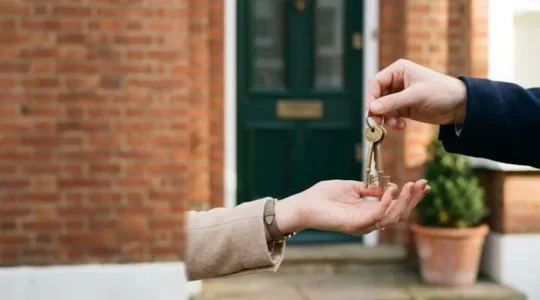 Close-up of a hand receiving house keys in front of a British home on completion day, symbolizing the legal transfer of property ownership