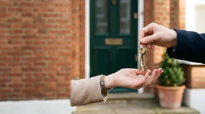 Close-up of a hand receiving house keys in front of a British home on completion day, symbolizing the legal transfer of property ownership